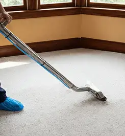 Steam carpet cleaning technician using a hot-water extraction wand on a residential carpet, wearing blue protective shoe covers Scottsdale, AZ.