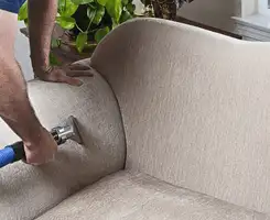 Professional upholstery cleaner deep-cleaning a fabric sofa with a handheld extraction tool and hose in Scottsdale, AZ.